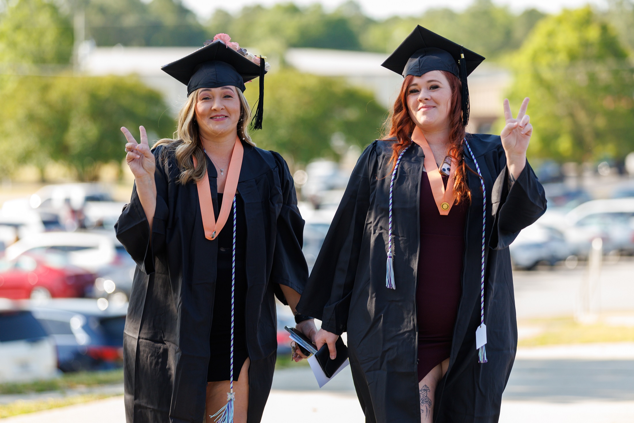 Two graduates hold up two fingers in a "peace sign" as they walk outside the Crown.