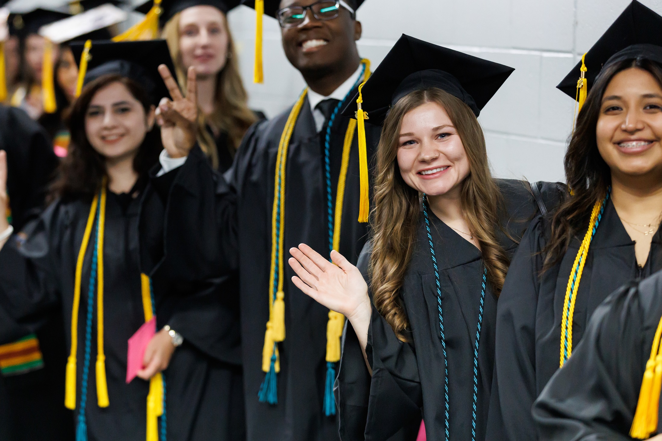 A group of graduates smile and wave at the camera while waiting in the hallway of the Crown.