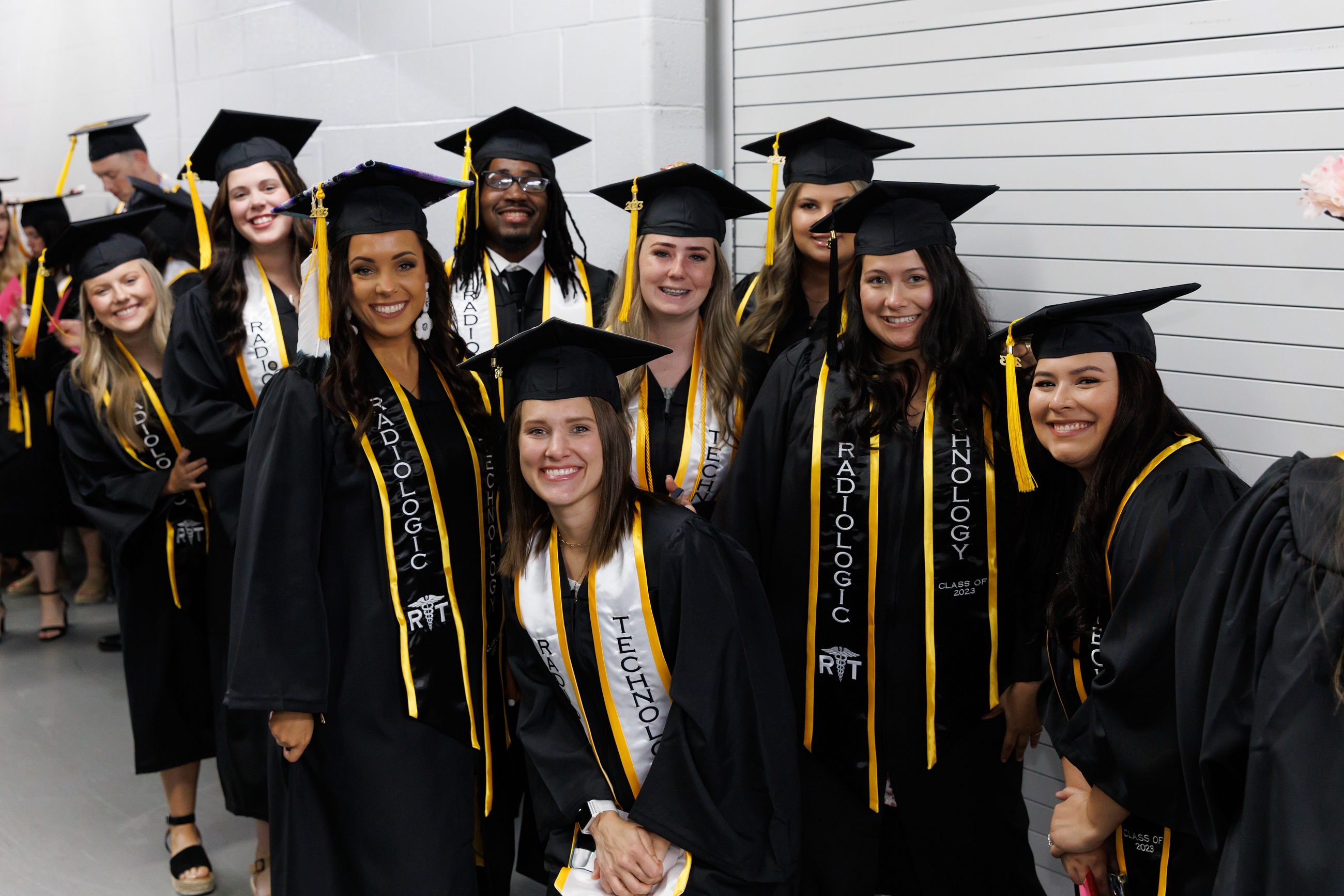 A group of graduates pose for a photo taken by a faculty member in the hallway of the Crown.