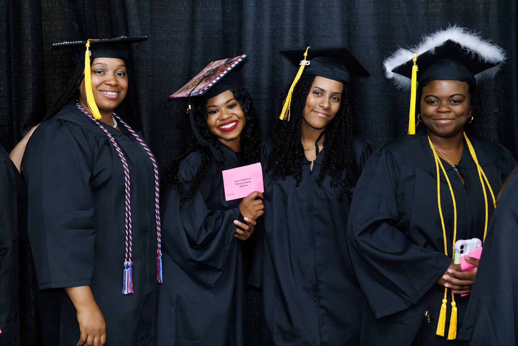 Four graduates smile for the camera while standing in front of a dark backdrop at the Crown.