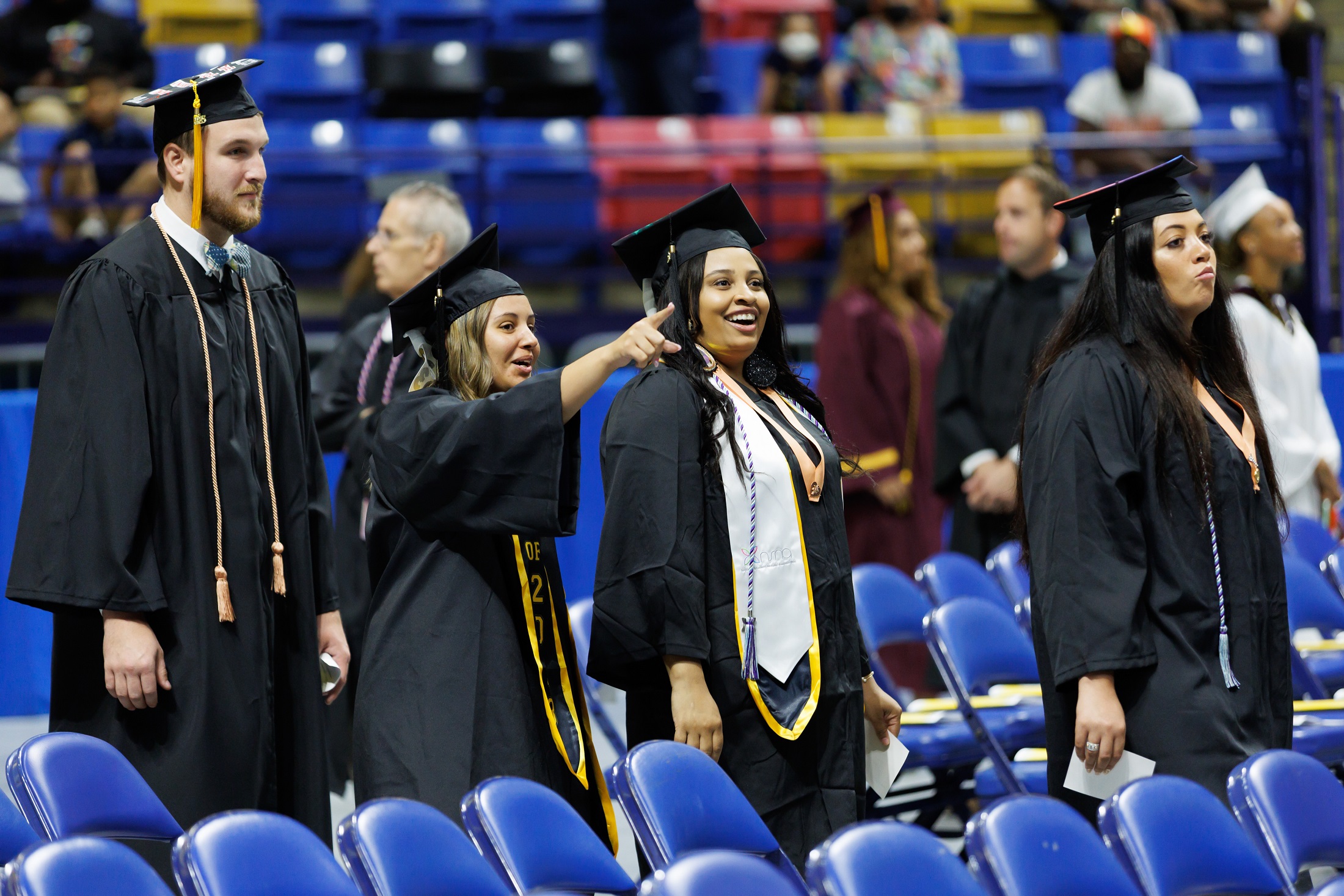 A graduate points up into the crown as she walks with her classmate in the processional line.