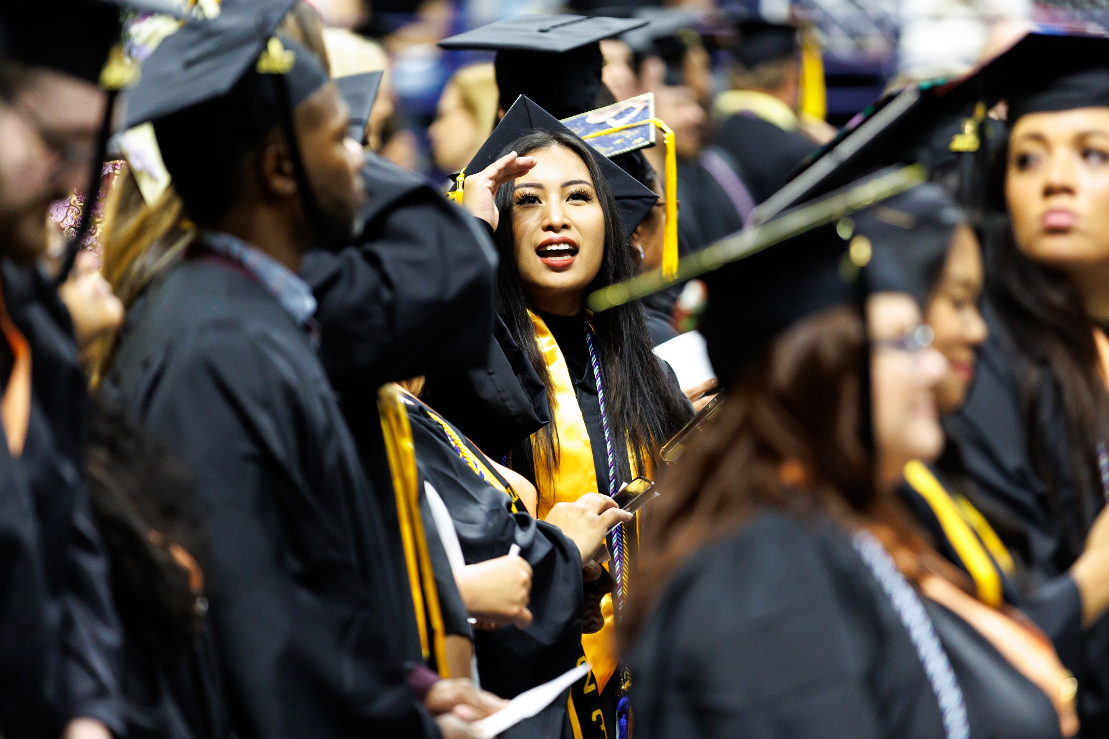 A graduate shields her eyes as she looks up into the crowd from the Crown floor.