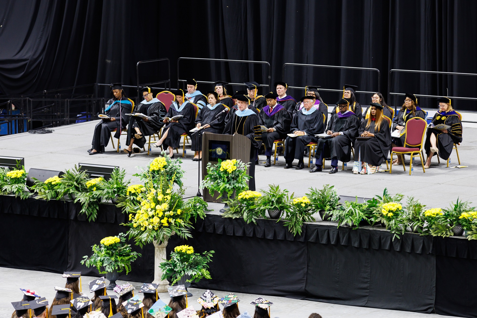 A photo of Dr. Mark Sorrells speaking at the podium and the distinguished guests seated on stage behind him.
