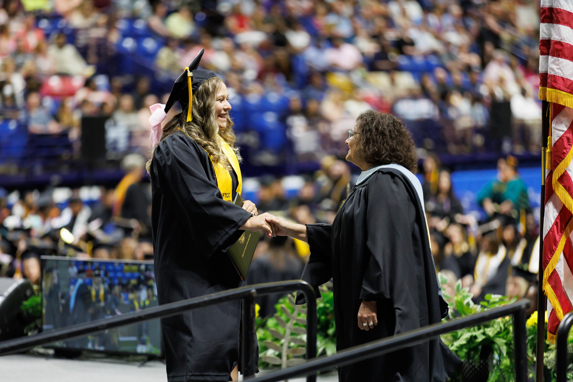 A graduate shakes hands with Michelle Walden as she crosses the stage.