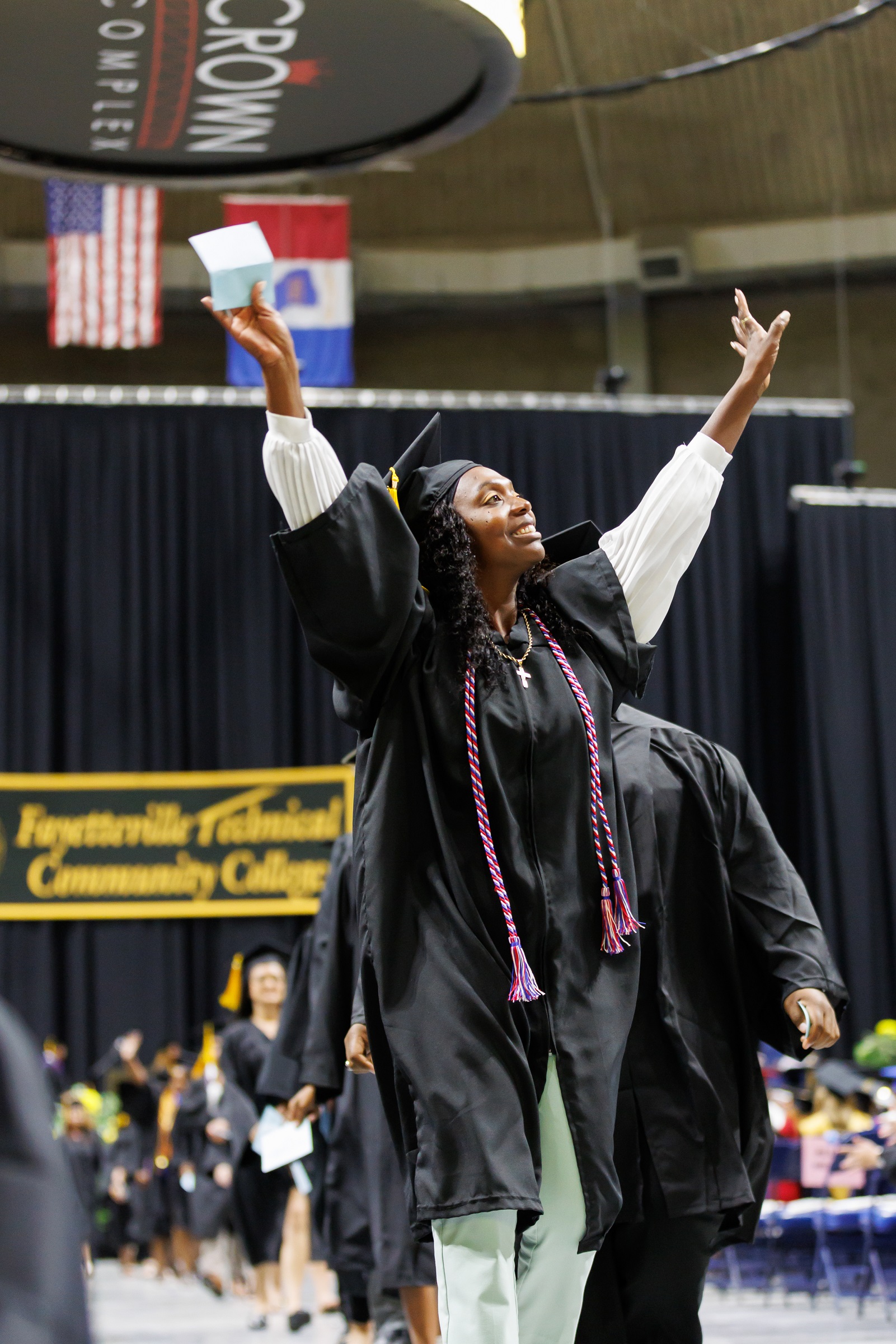 A graduate lifts both hands in celebration as she walks to cross the stage.