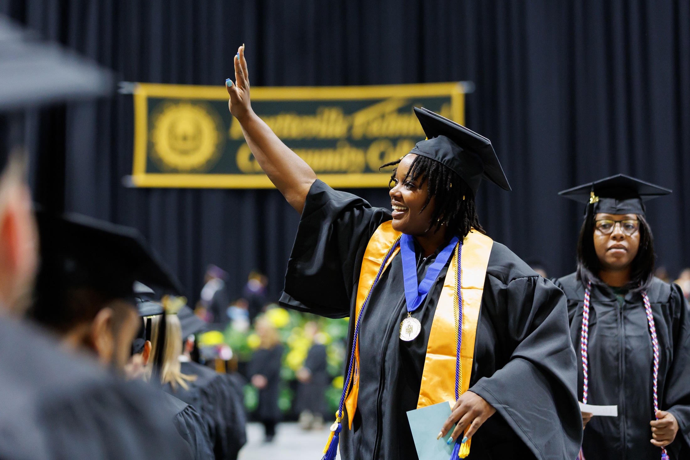 A graduate waves to the crowd as she walks to cross the stage.