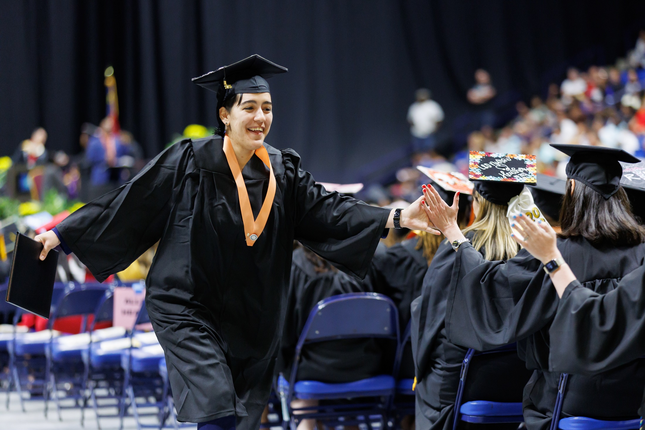 A graduate walking down the center aisle high-fives a seated graduate.