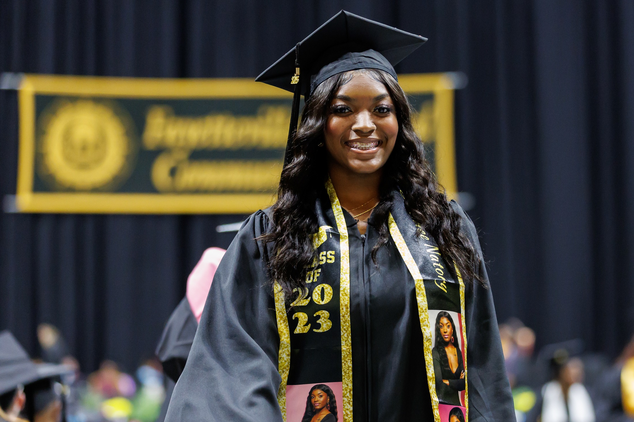 A graduate wearing a personalized stole smiles at the camera as she returns to her seat.