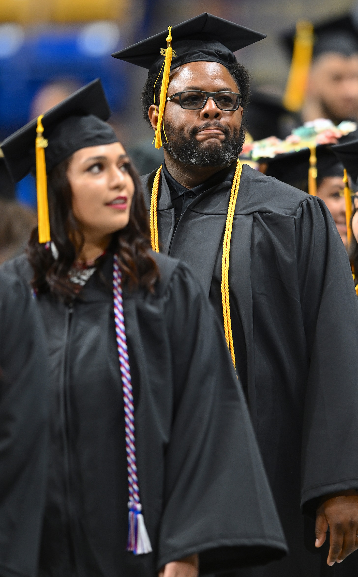 A bearded graduate wearing black-rimmed glasses walks in the processional line.