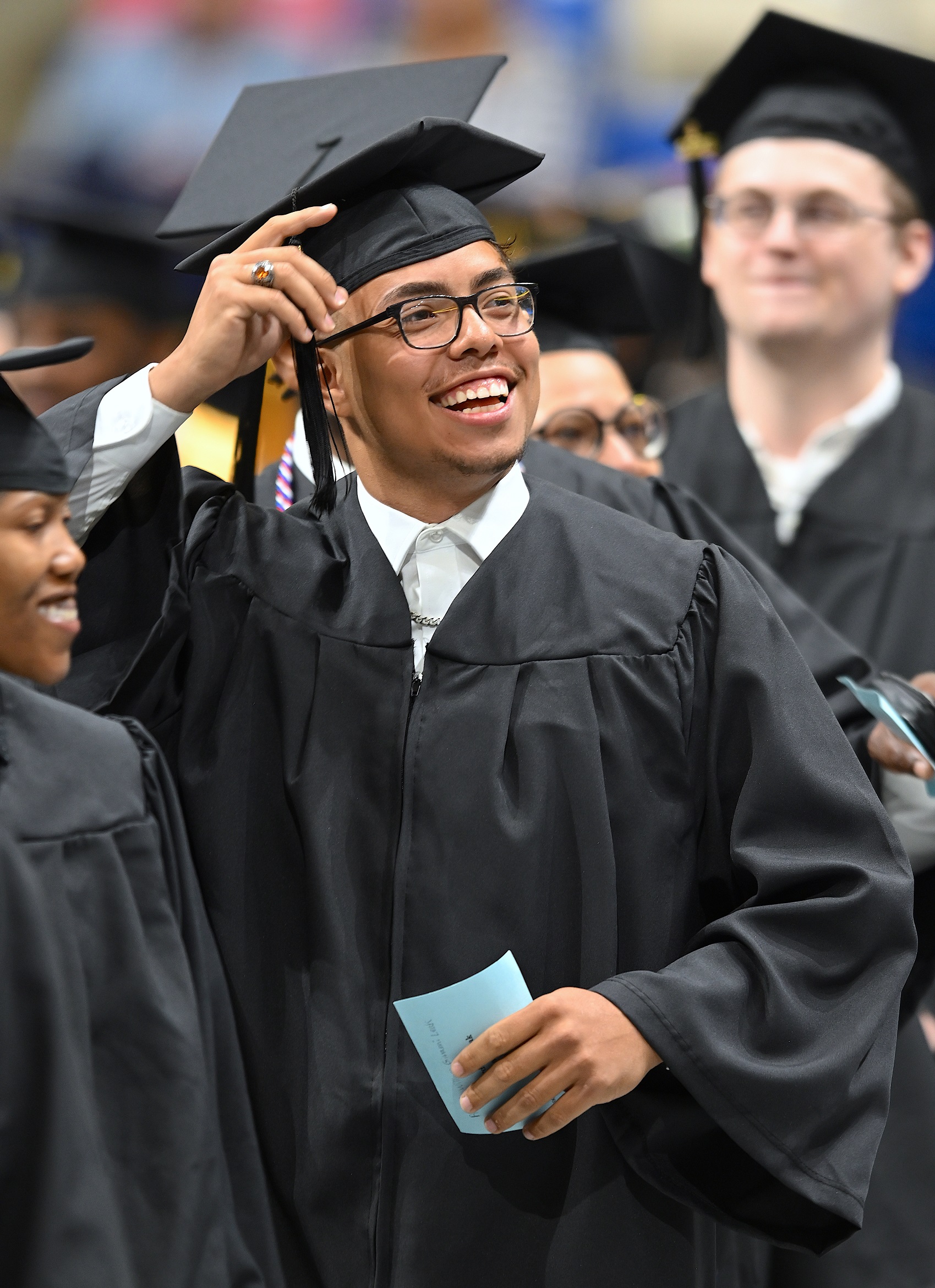 A graduate wearing glasses smiles and raises his hand has he enters the Crown floor.