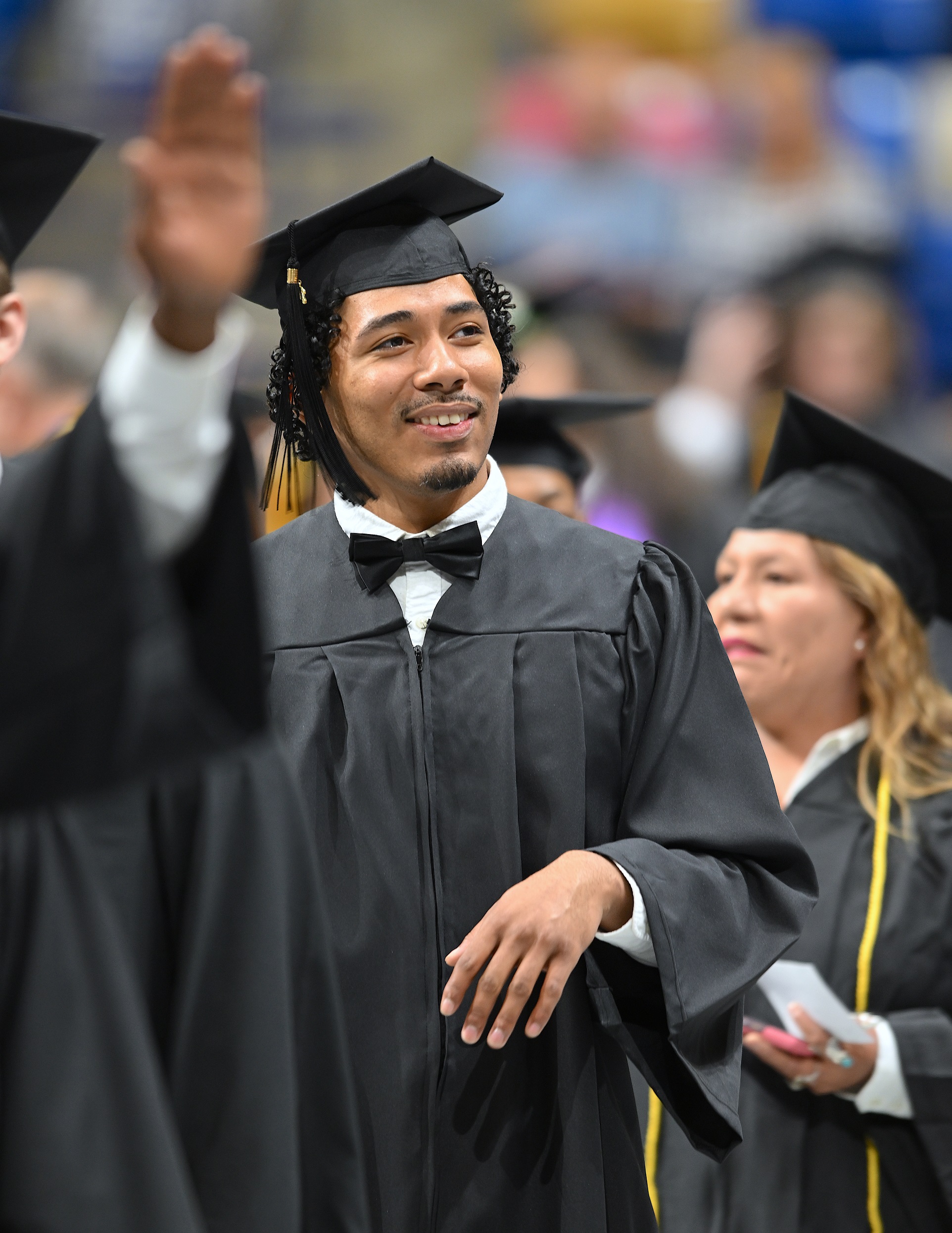 A graduate in a bow tie smiles as he walks in the processional line.