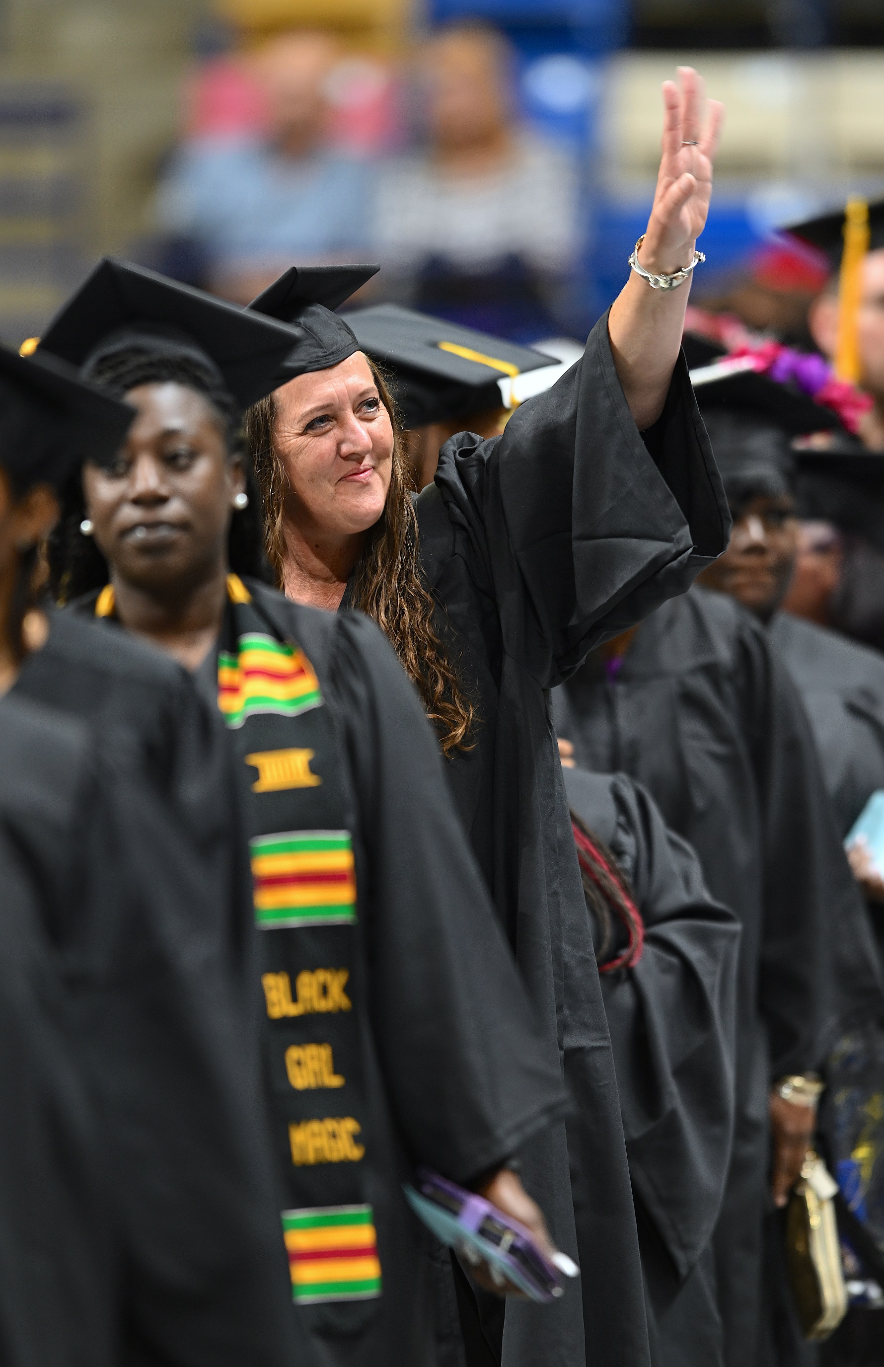 A graduate waves to someone in the crowd as she walks in the processional line.