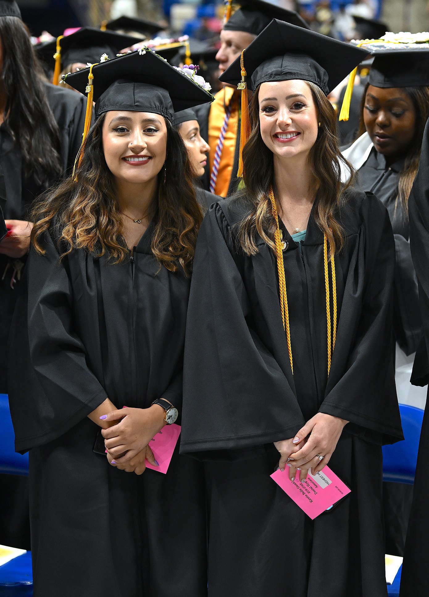 Two graduates smile for the camera as they stand by their seats.