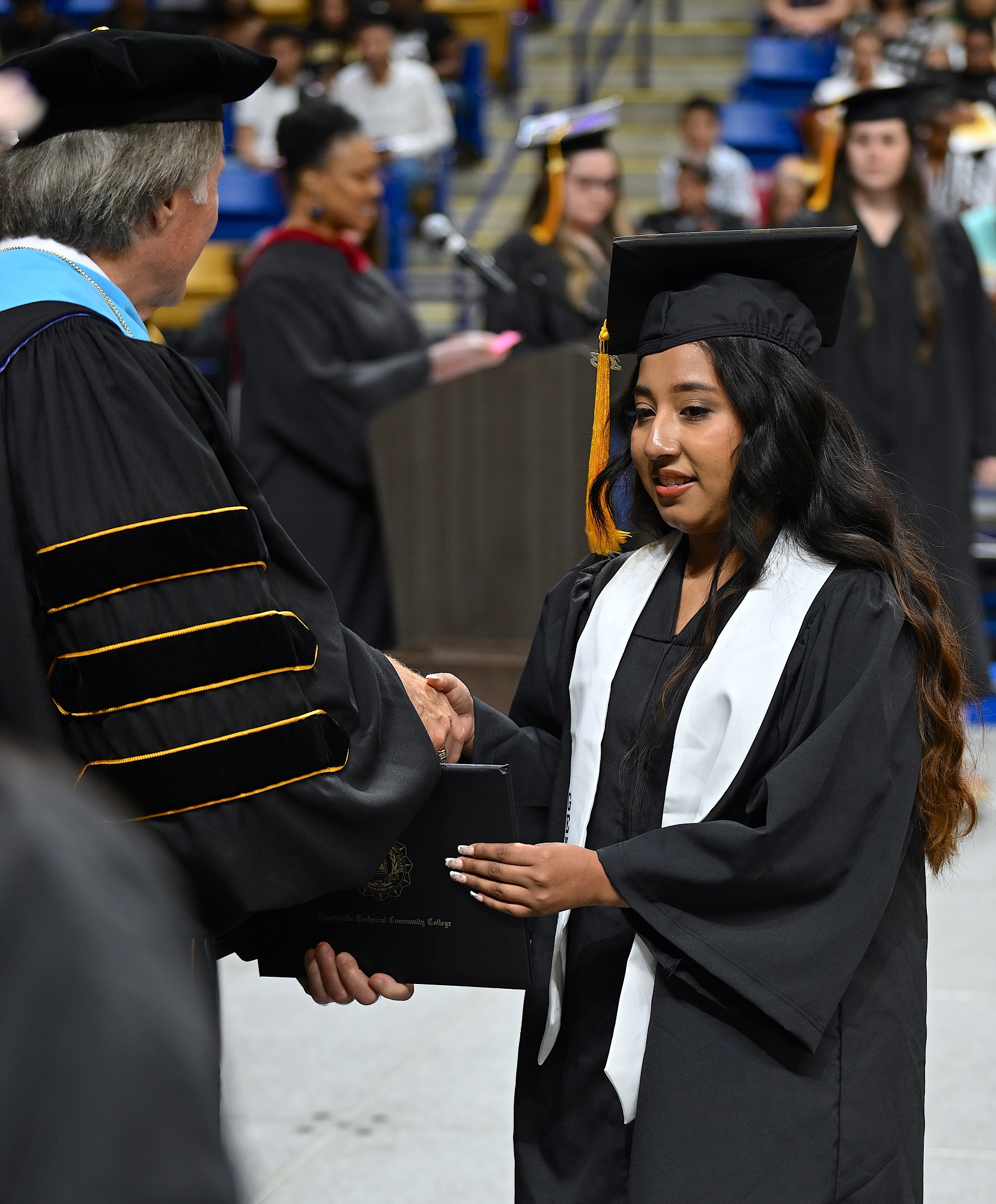 A graduate wearing a white stole accepts her diploma folder from Dr. Mark Sorrells.