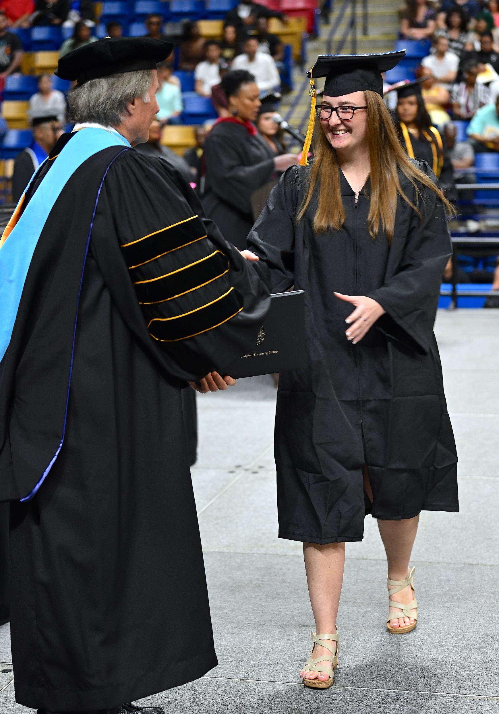 A graduate smiles at Dr. Mark Sorrells as she reaches for her diploma folder.