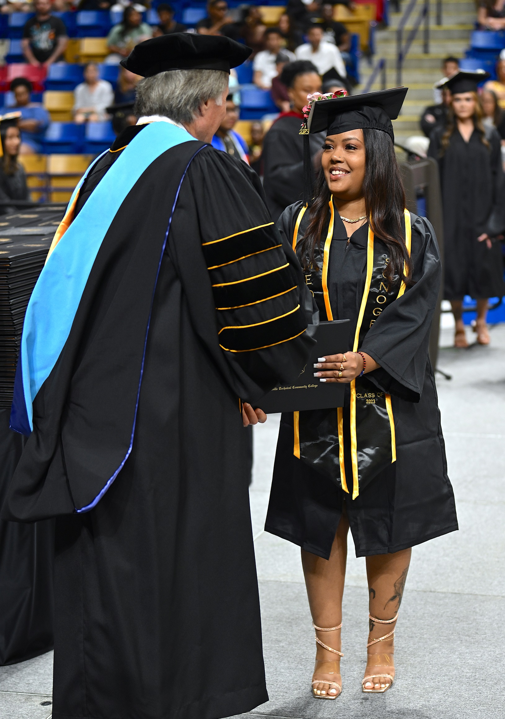 A graduate wearing a black and gold medical sonography stole smiles at Dr. Mark Sorrells as she accepts her diploma folder.