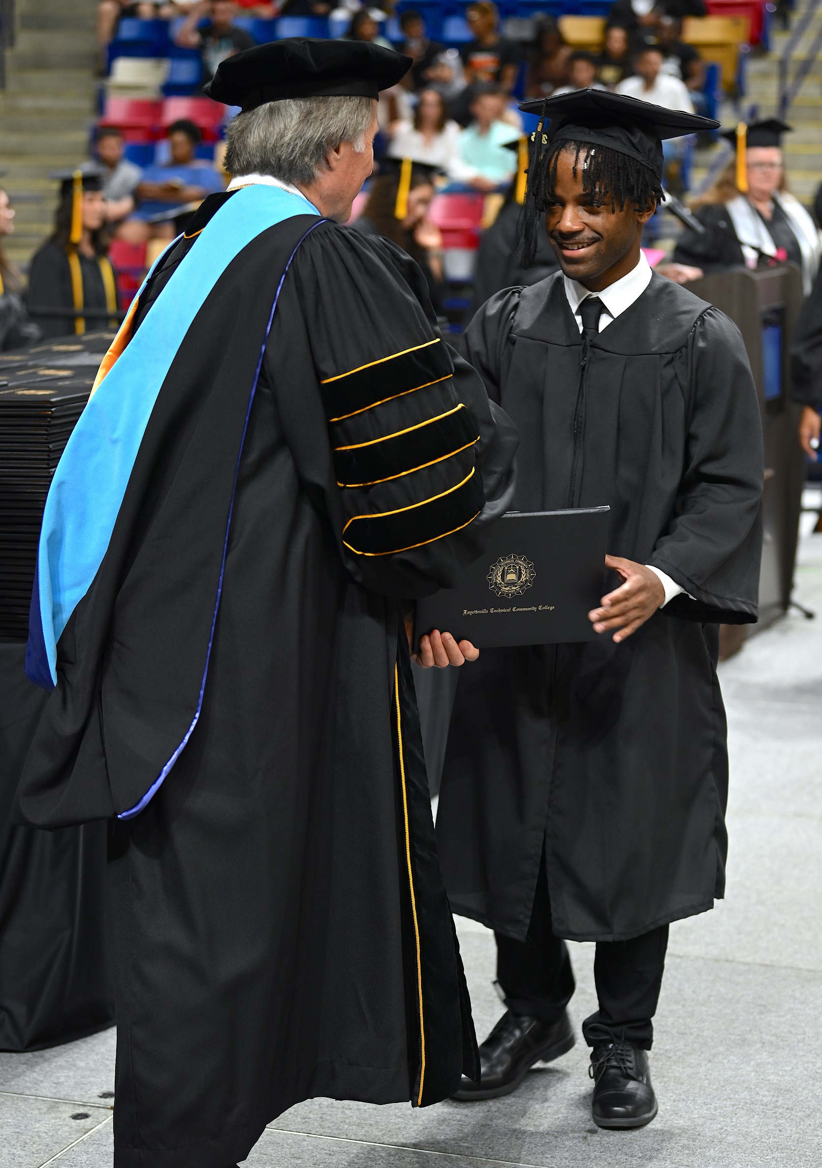 A graduate in a black necktie accepts his diploma folder from Dr. Mark Sorrells.
