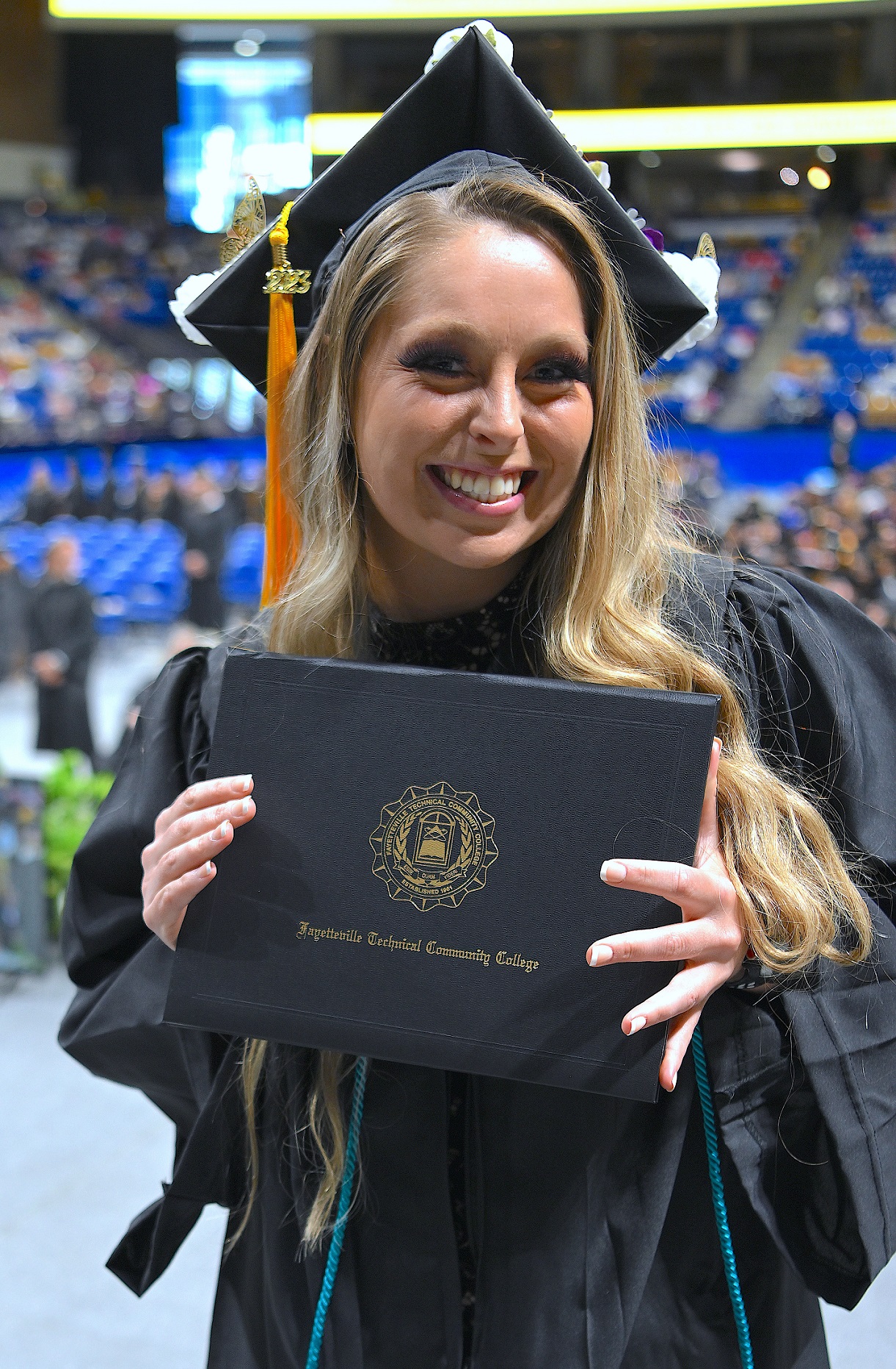 A close-up photo a graduate smiling while holding up her diploma folder.