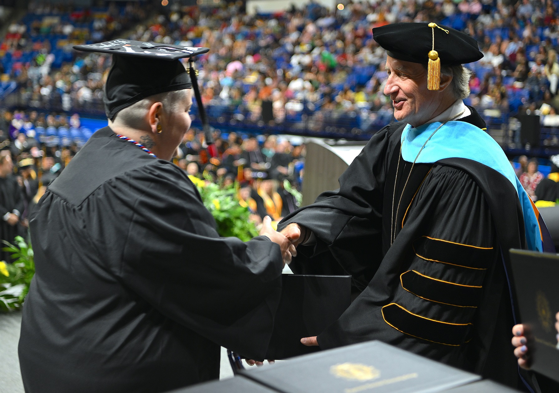 A graduate with short hair shakes hands with Dr. Mark Sorrells as she accepts her diploma folder from him.