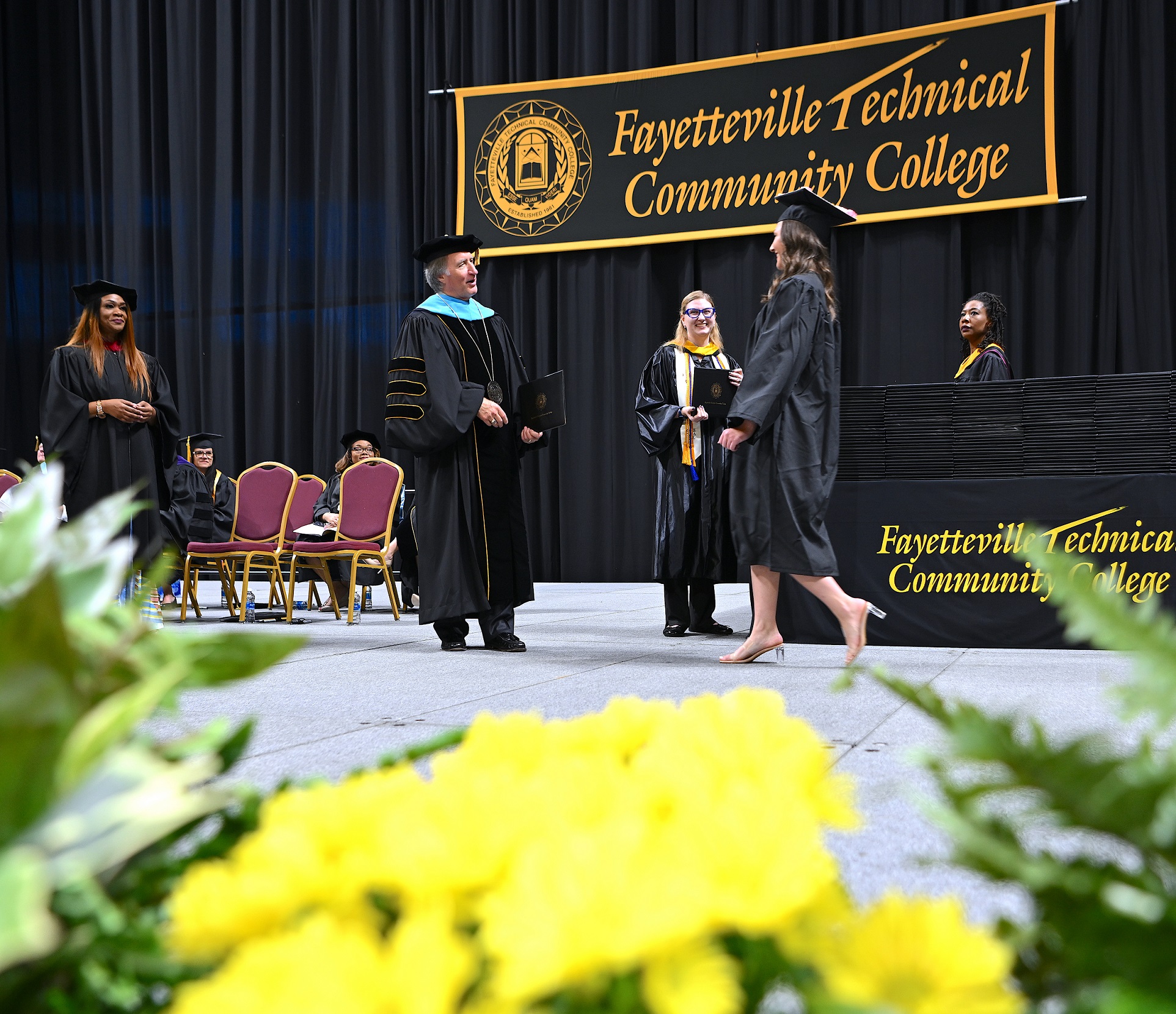 A wide shot of the stage as a graduate approaches Dr. Mark Sorrells to receive her diploma folder.