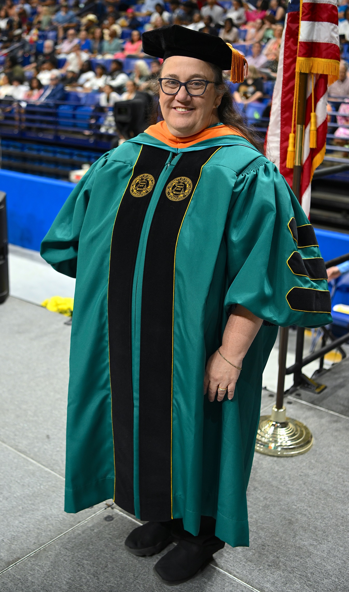 A faculty member in green and black graduation regalia poses for the camera.