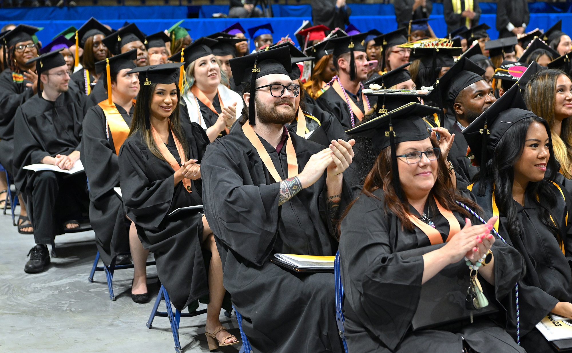 Graduates seated in rows clap during the commencement ceremony.