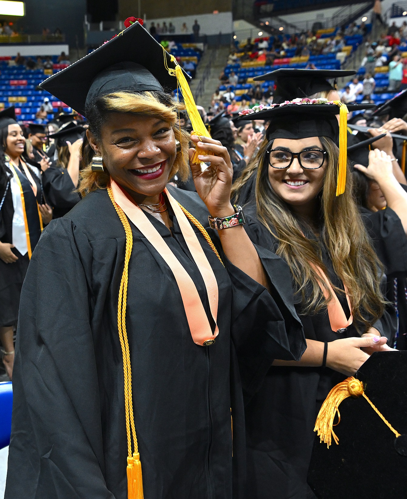 Two graduates wearing peach-colored pin ribbons smile at the camera.