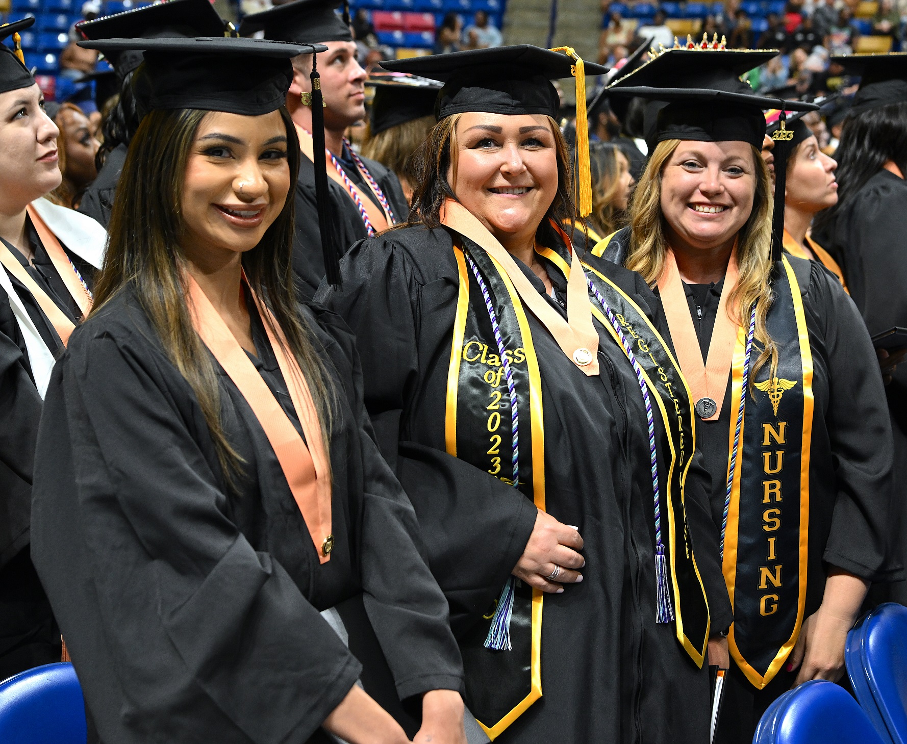 Graduates in a row stand up and smile at the camera.