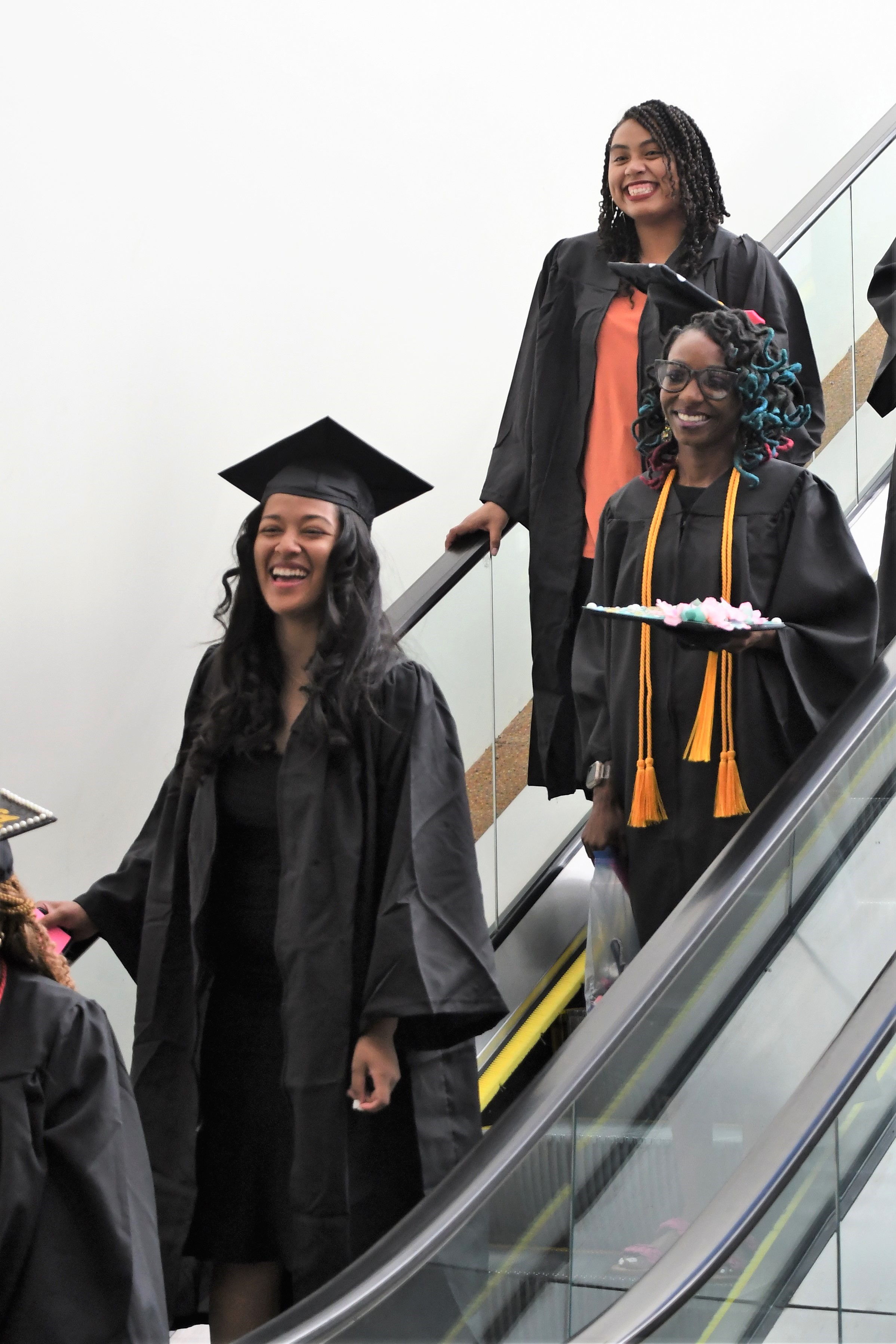 Graduates smile at the camera as they descend the escalator. 