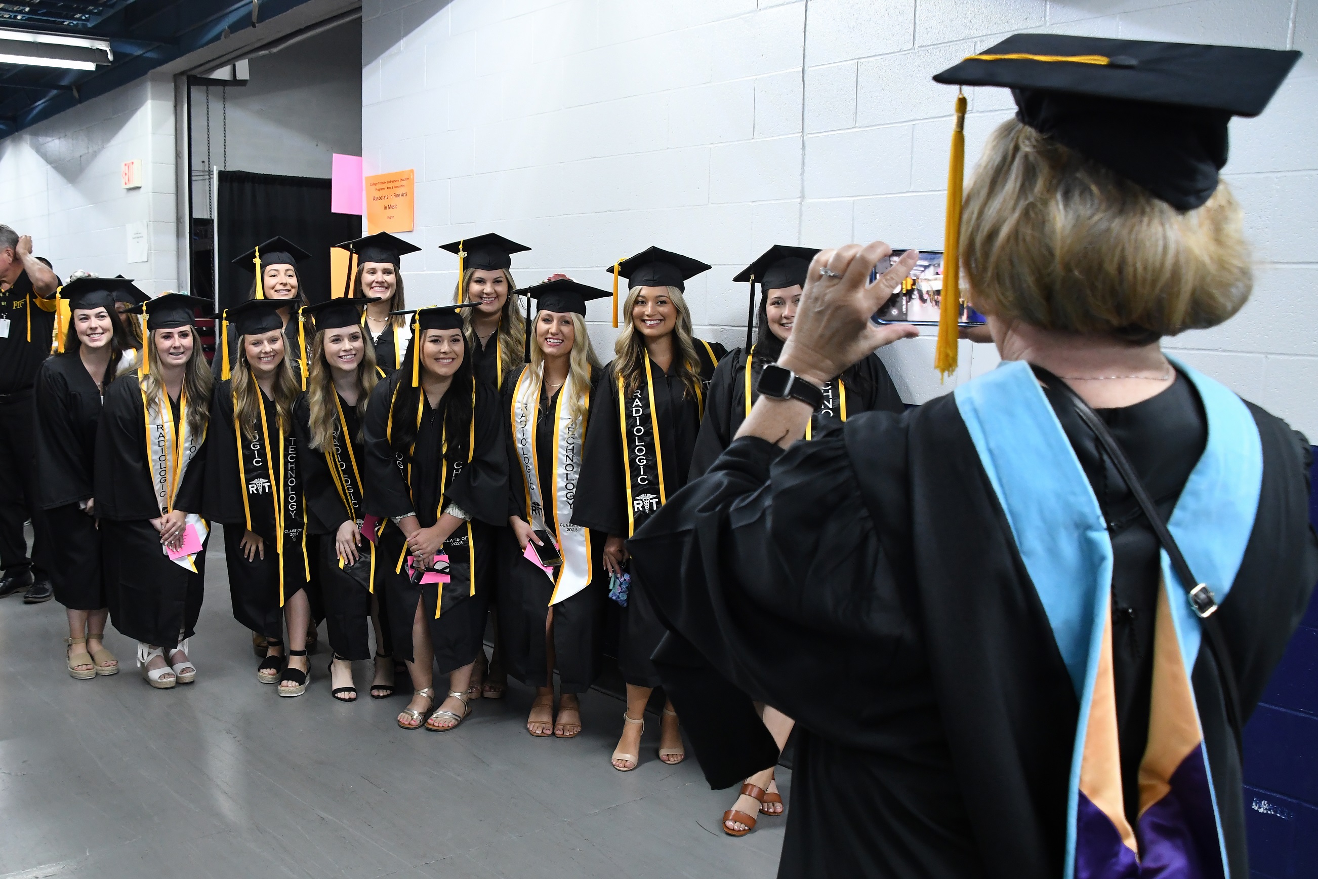 A group of graduates pose for a photo being taken by a faculty member.