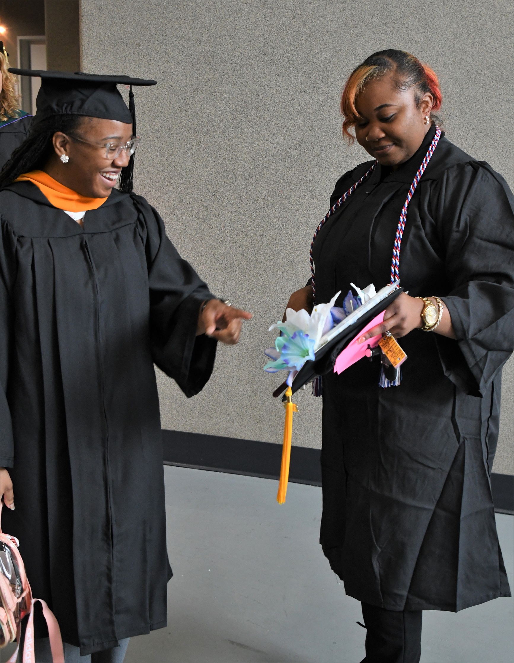 A faculty member points at a cap held by a graduate in the hallway of the Crown.
