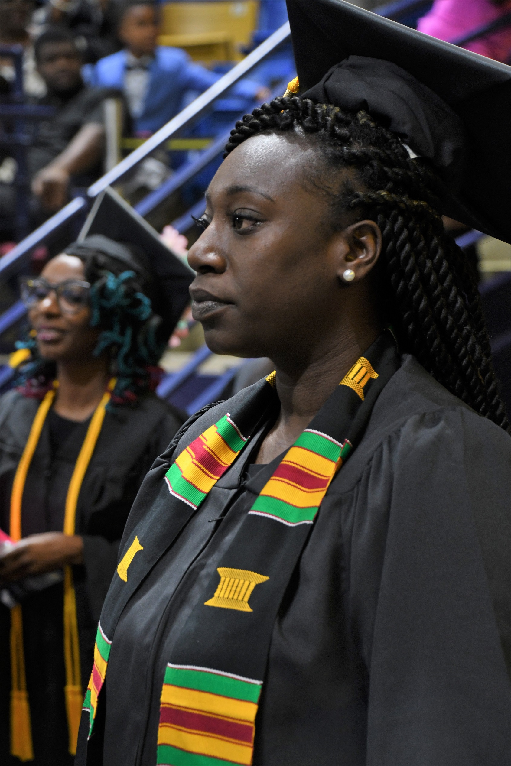 A close-up photo of a graduate wearing a black, green, yellow and red stole.