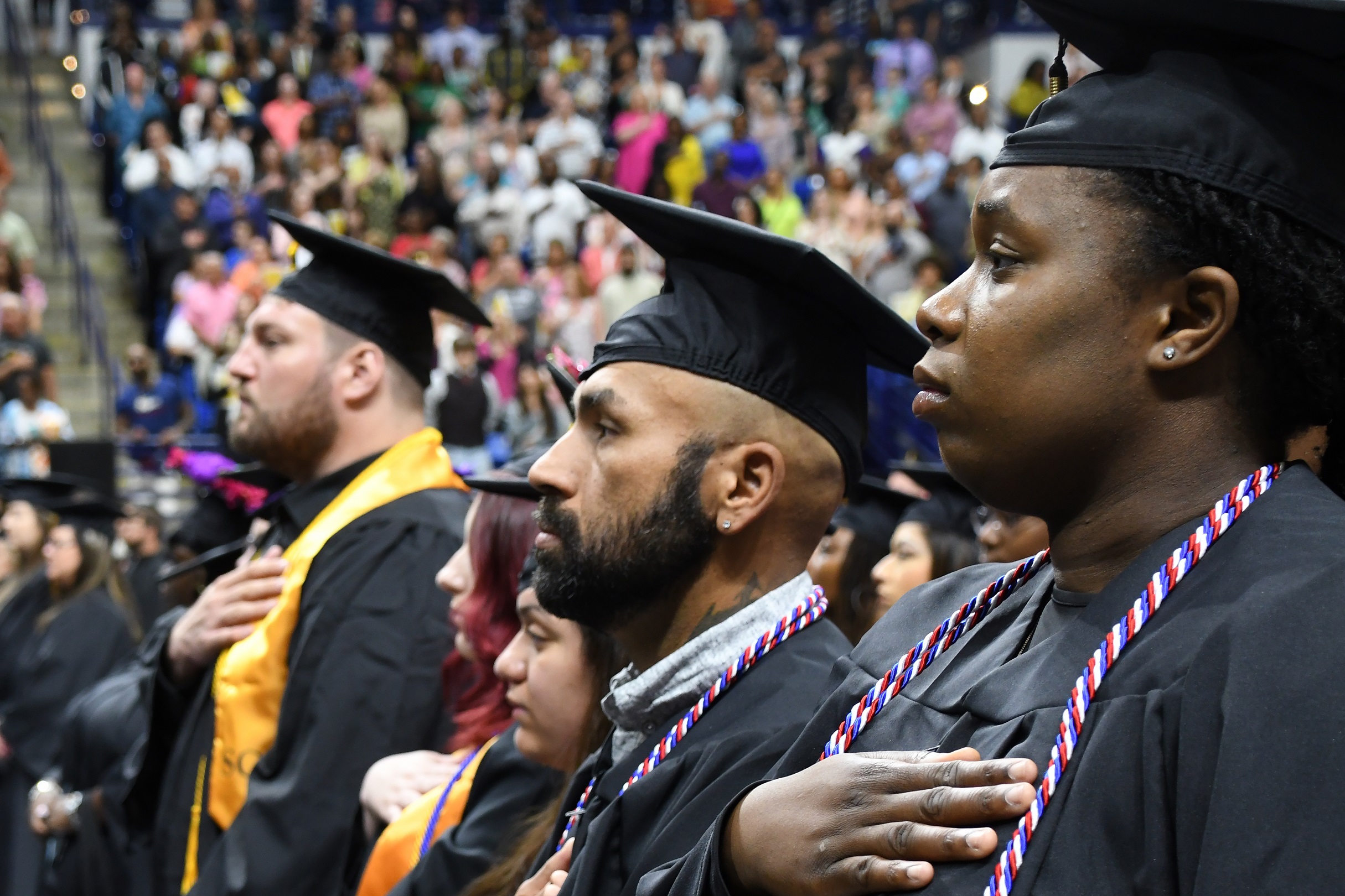 Graduates stand with their hands over their hearts.