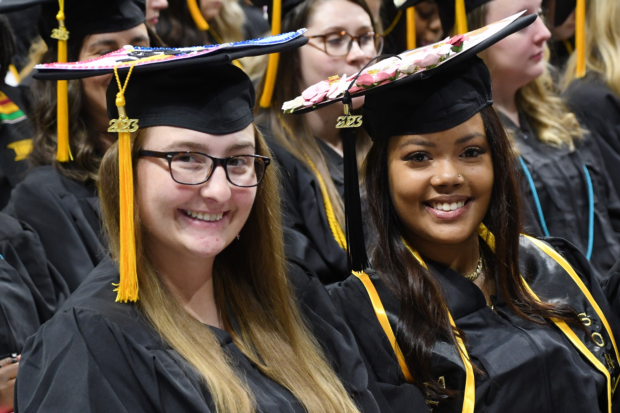 Two graduates seated next to each other smile at the camera during Commencement.