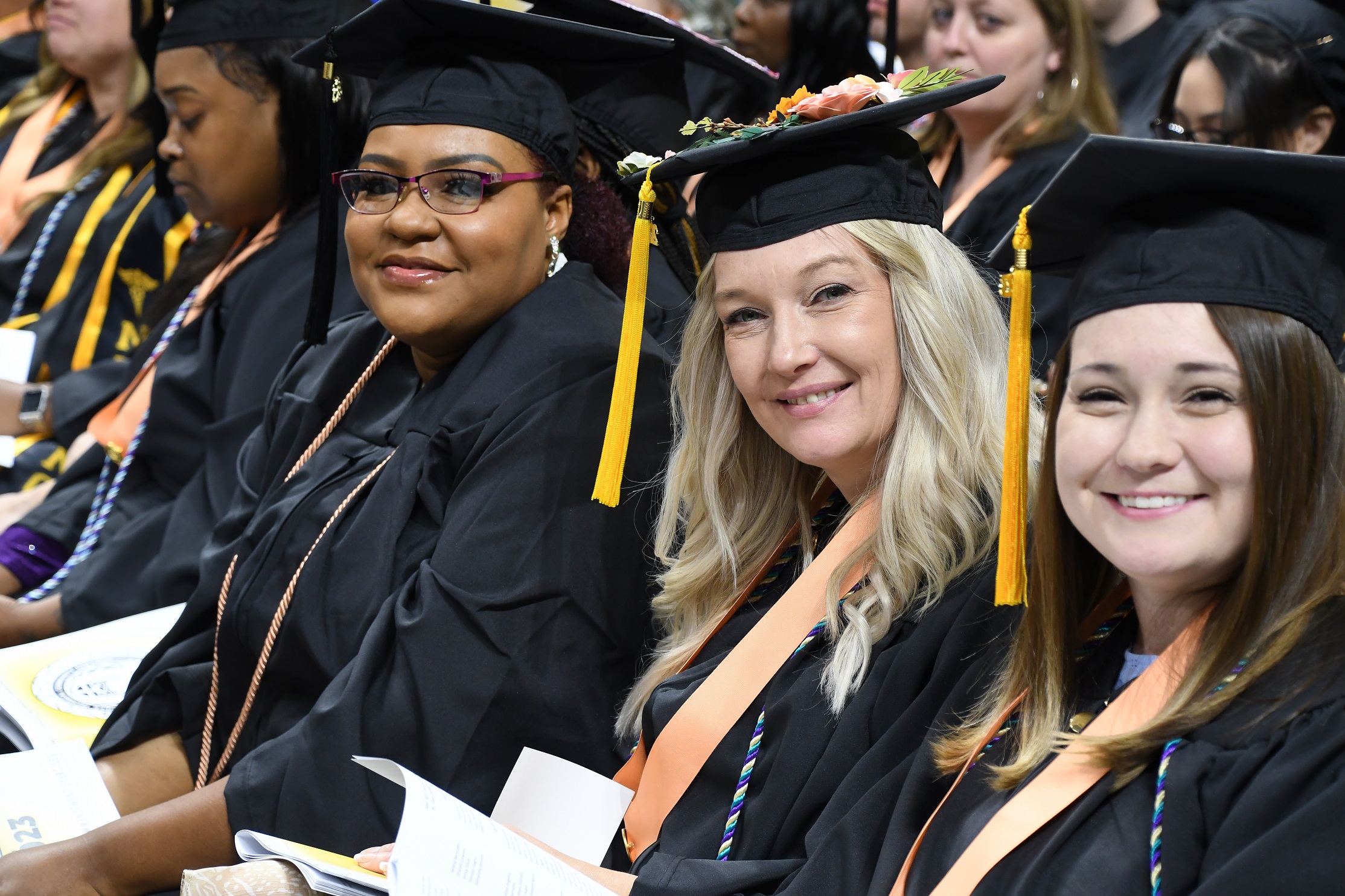 Graduates sitting in a row smile at the camera.