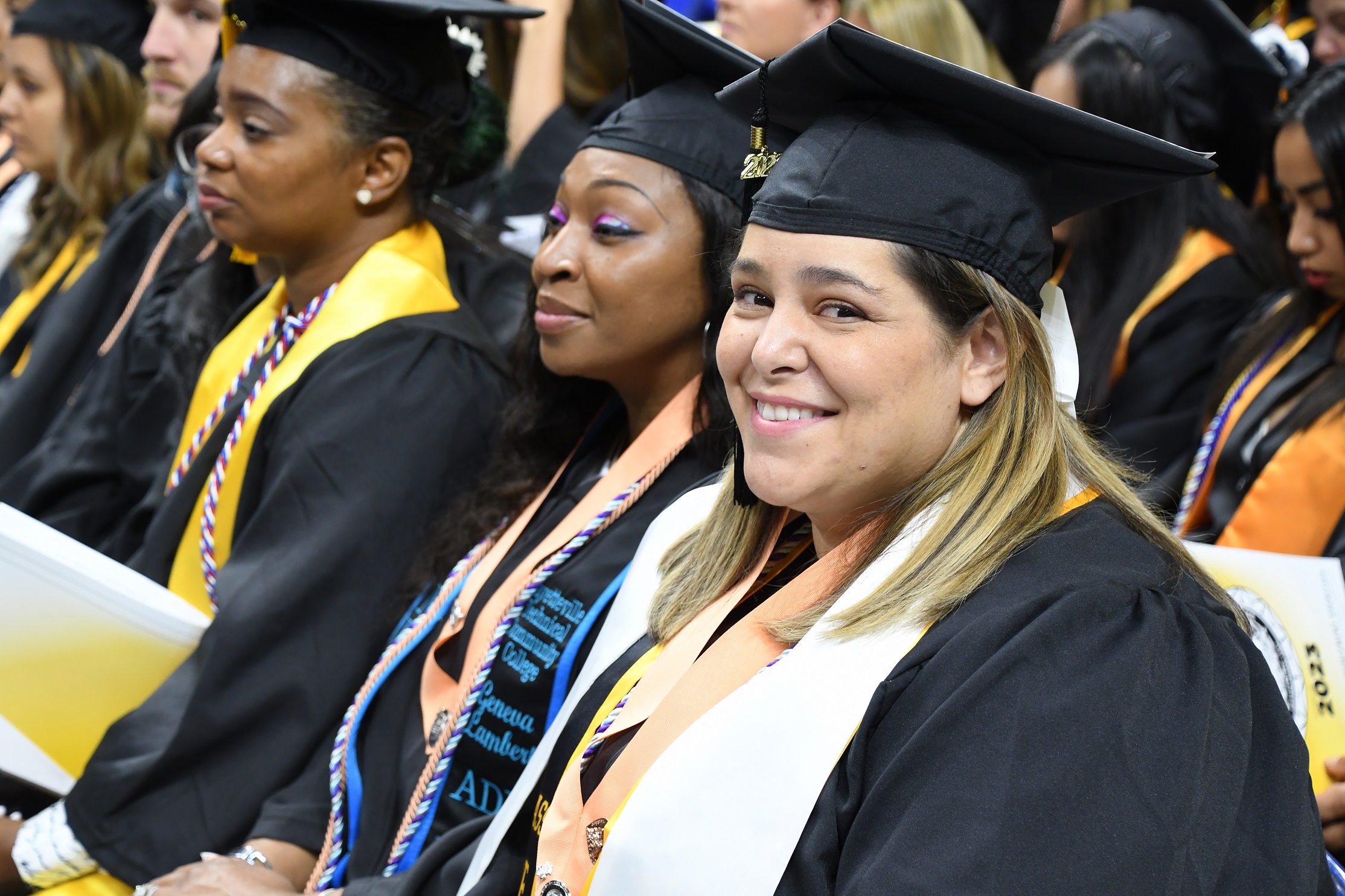 A graduate wearing a white stole and a pin ribbon smiles at the camera.
