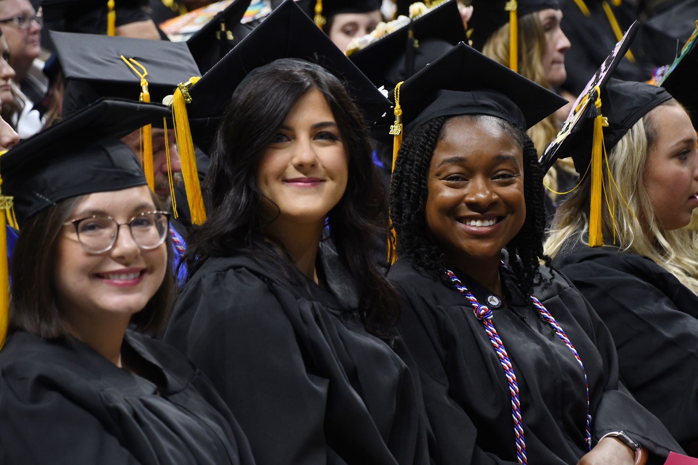 Graduates sitting in a row smile at the camera.