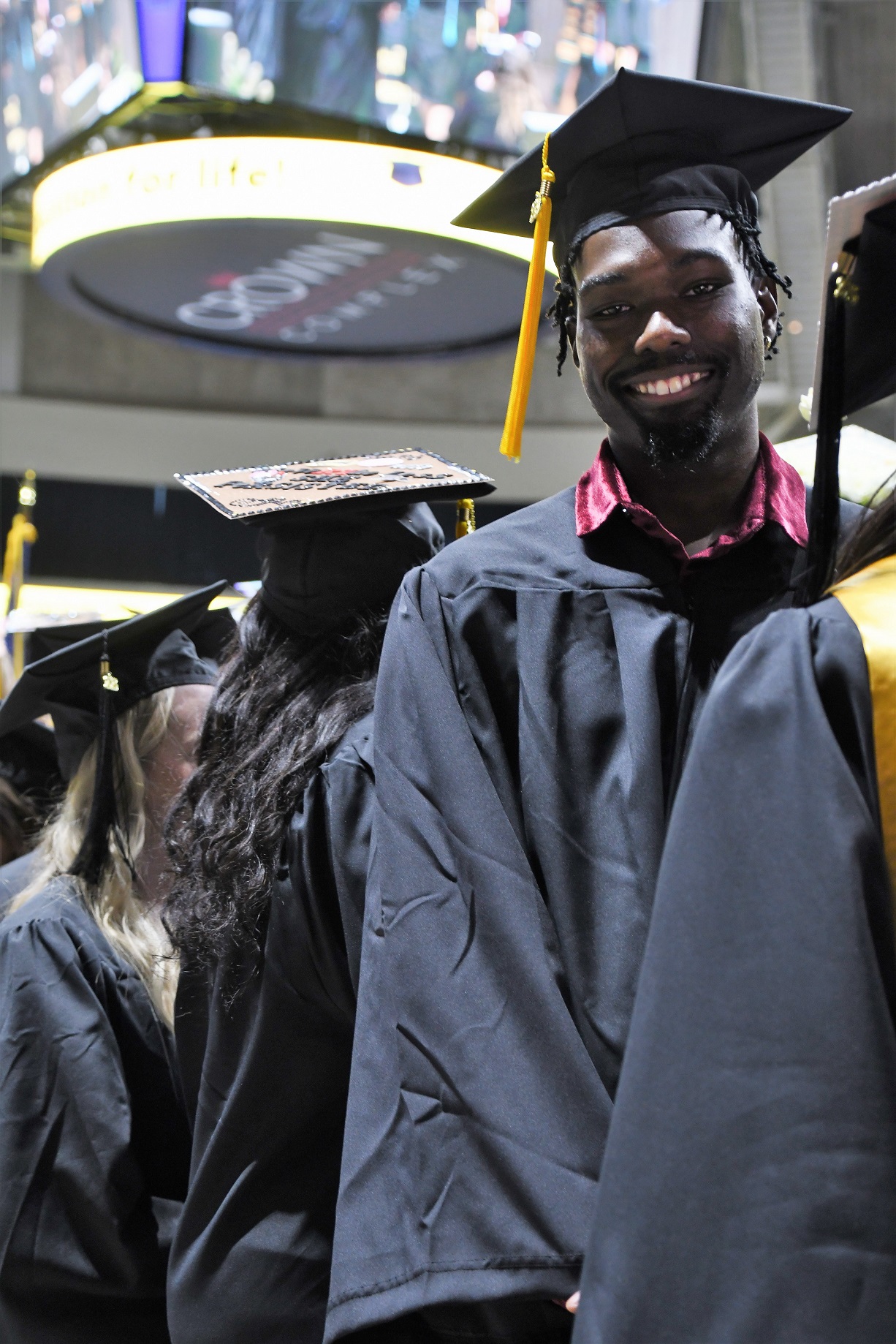 A graduate leans out of the processional line to smile at the camera.