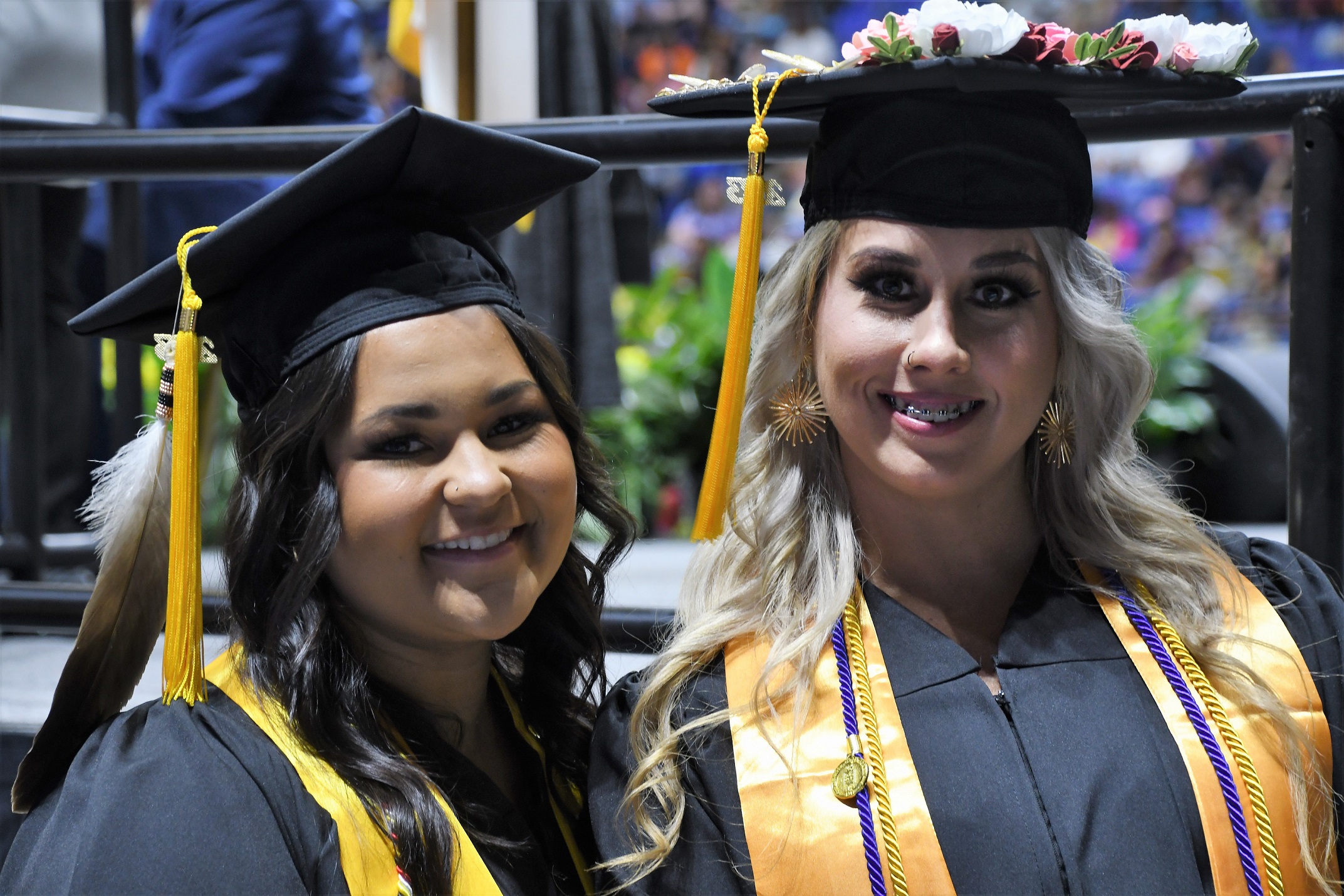 Two graduates wearing yellow stoles smile at the camera.