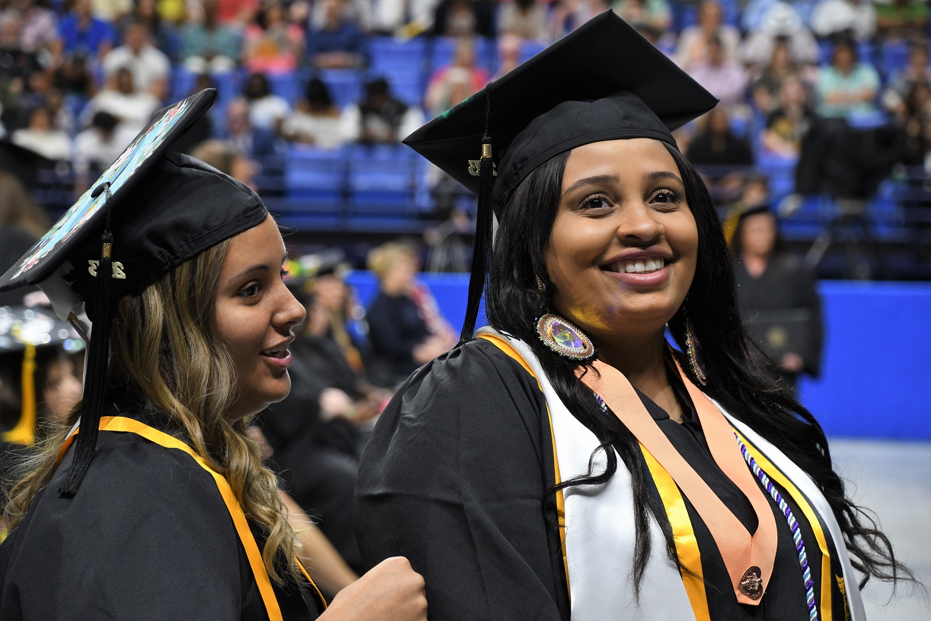 A graduate wearing a white stole and a peach-colored ribbon with a pin smiles at the camera.