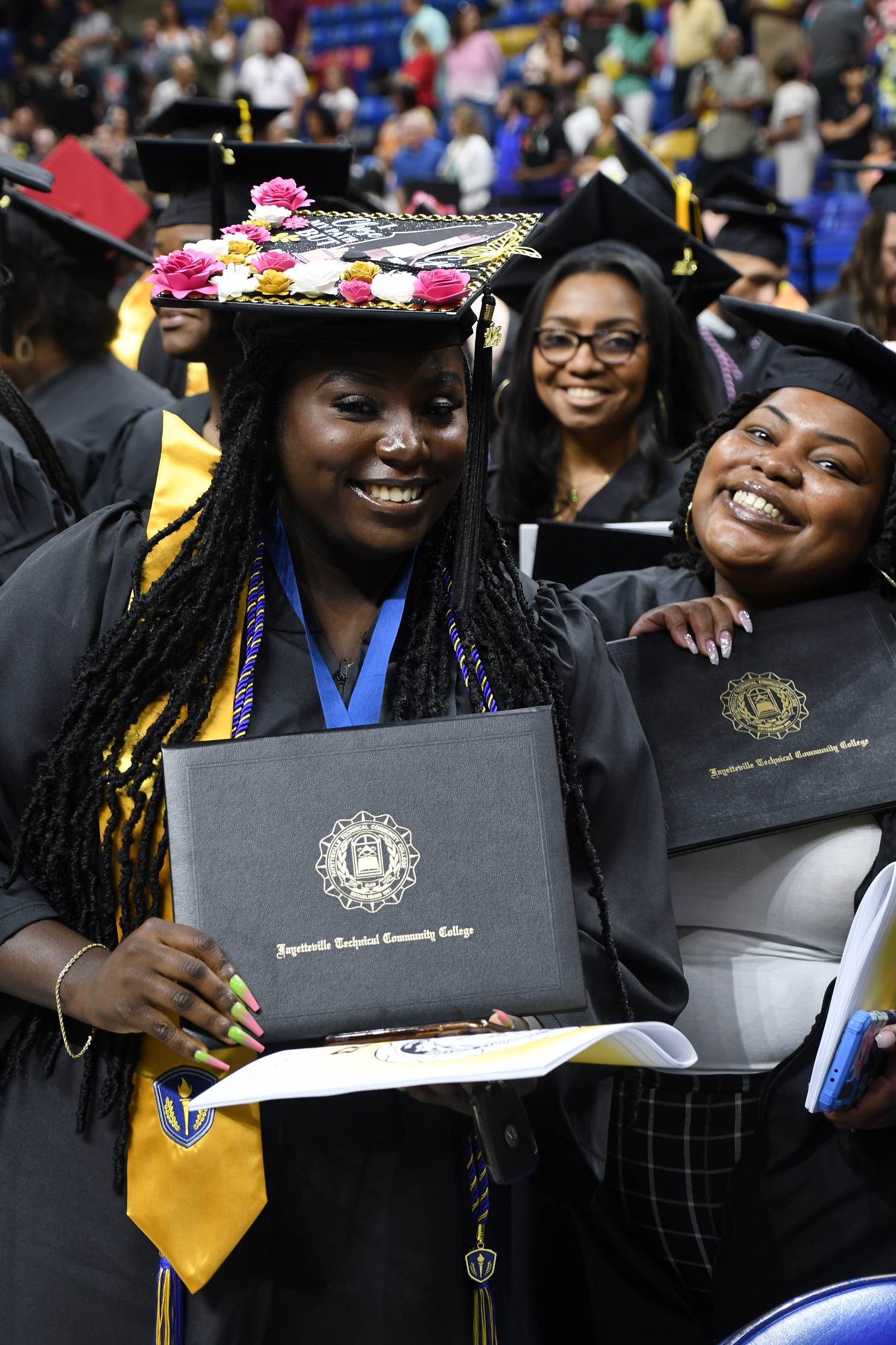 Graduates smile as they hold up their diploma folders.