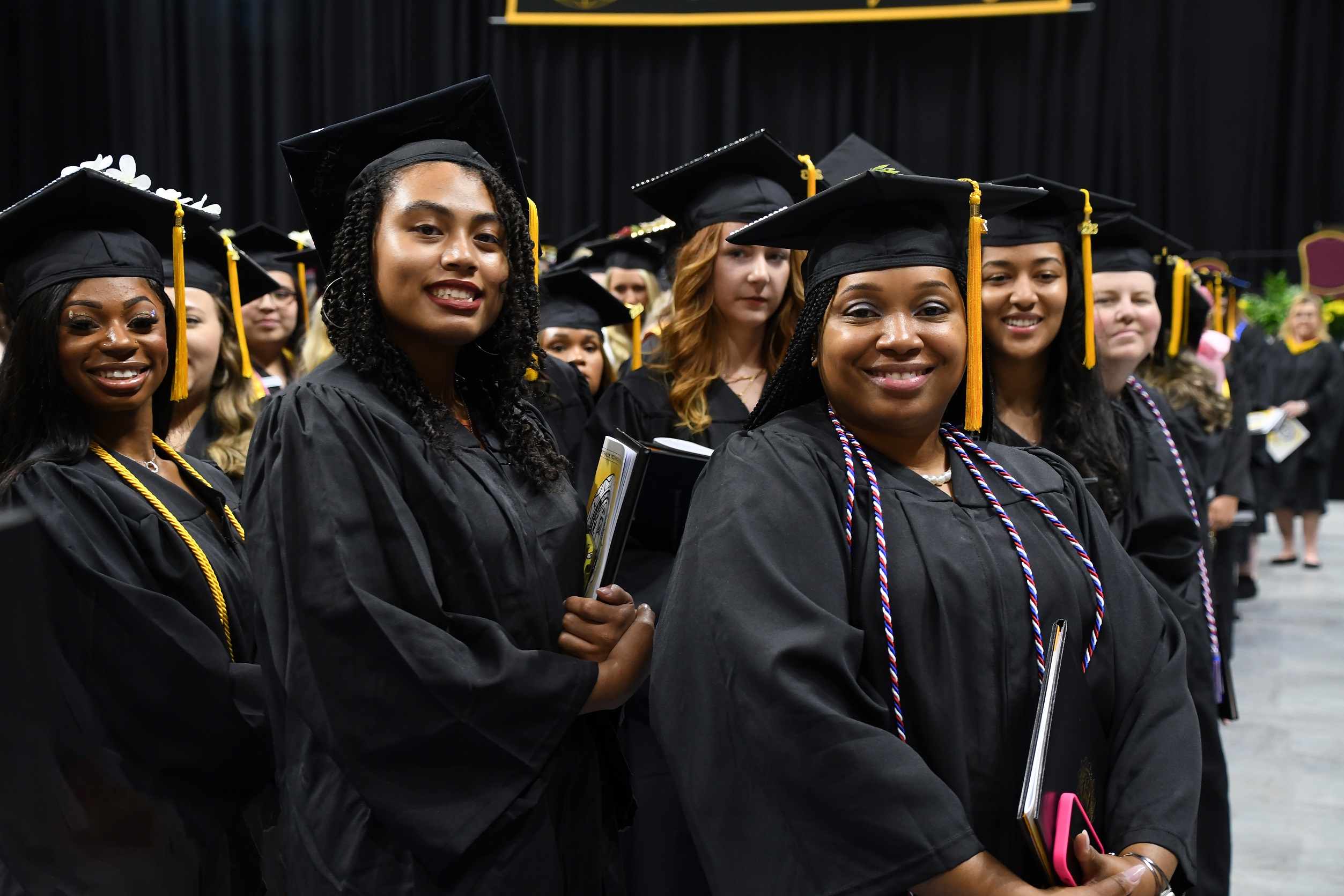 A group of graduates turn toward the camera and smile as they stand by their seats on the Crown floor.