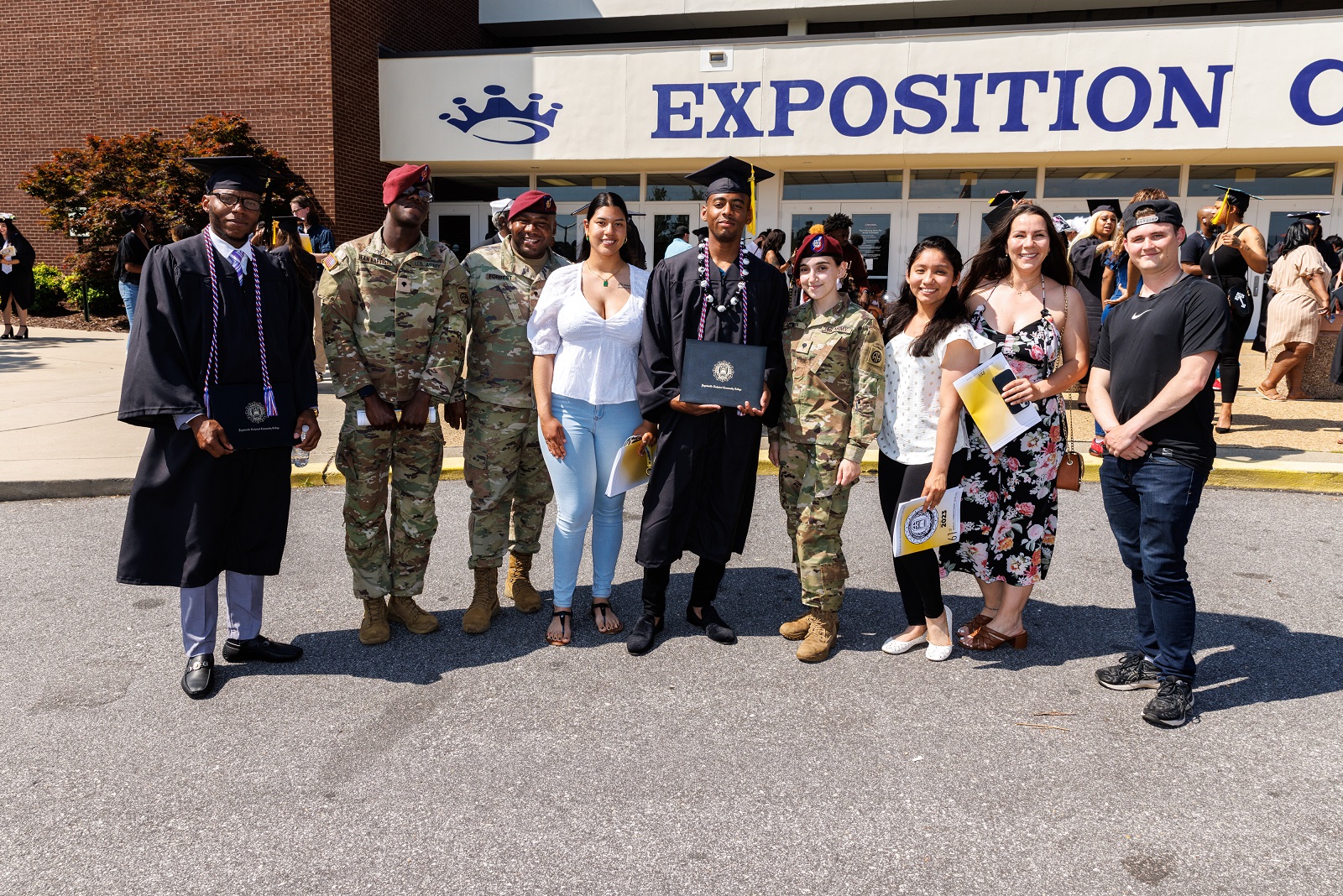 A group of graduates and friends, some of them in military uniform, stand together for a photo outside of the Crown.