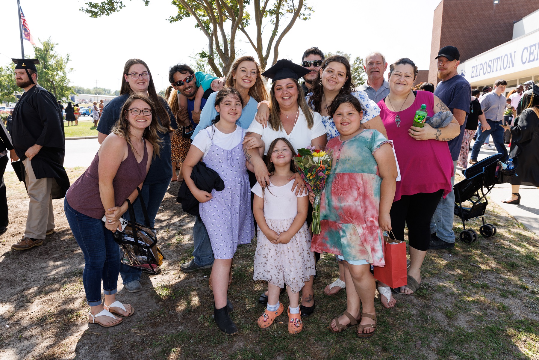 A graduate poses with a large group of her loved ones outside.
