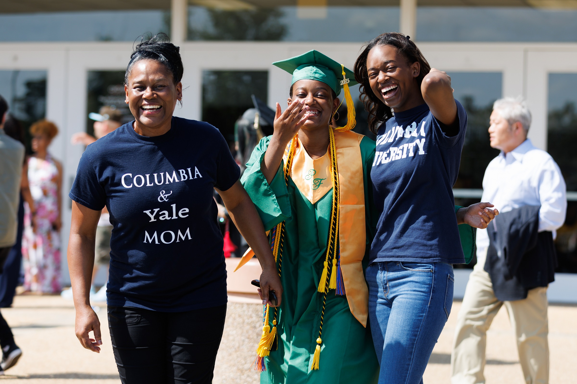 A graduate in a green cap and gown and gold stole poses with two women.