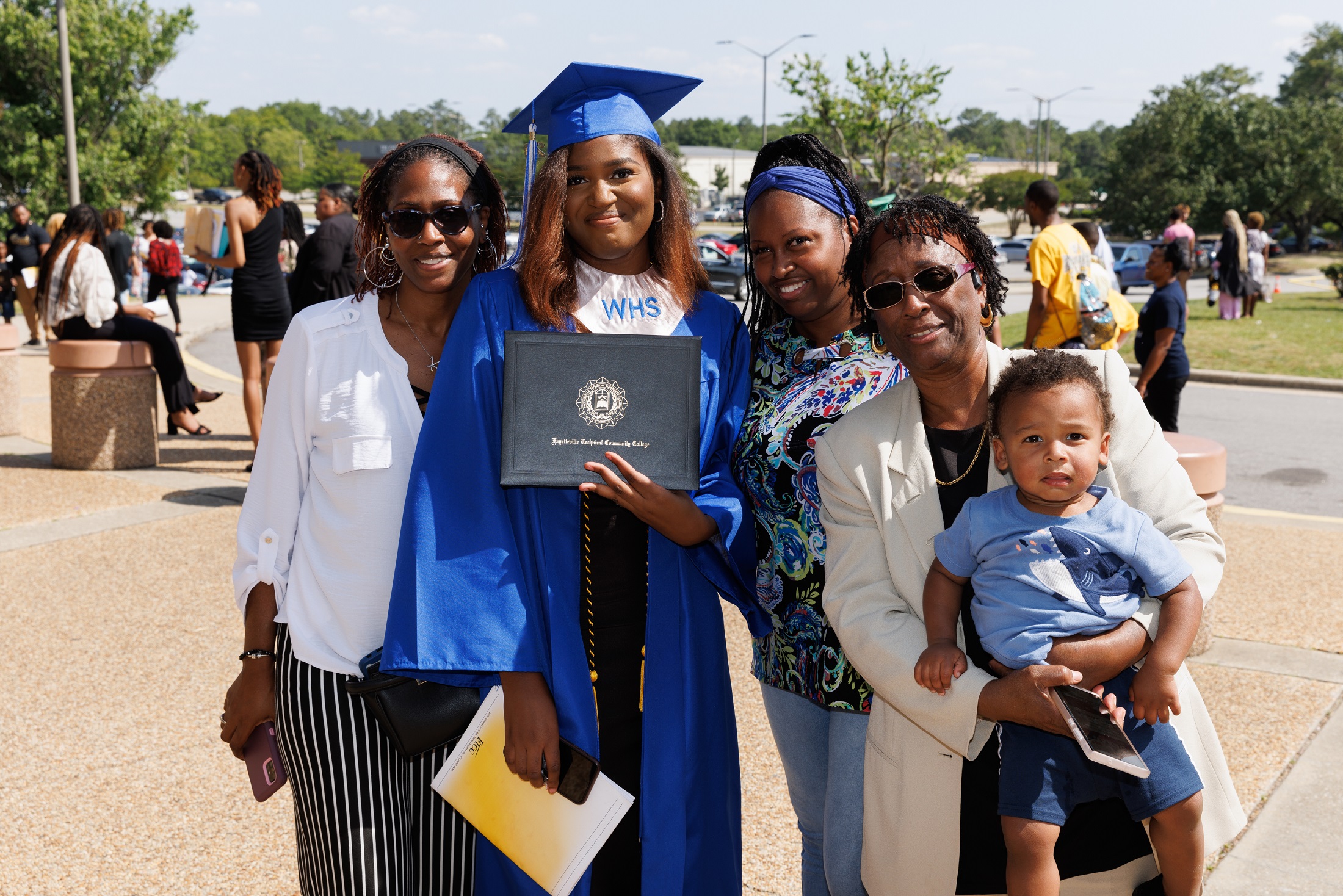 A graduate wearing a blue cap and gown and a silver stole poses with her loved ones.