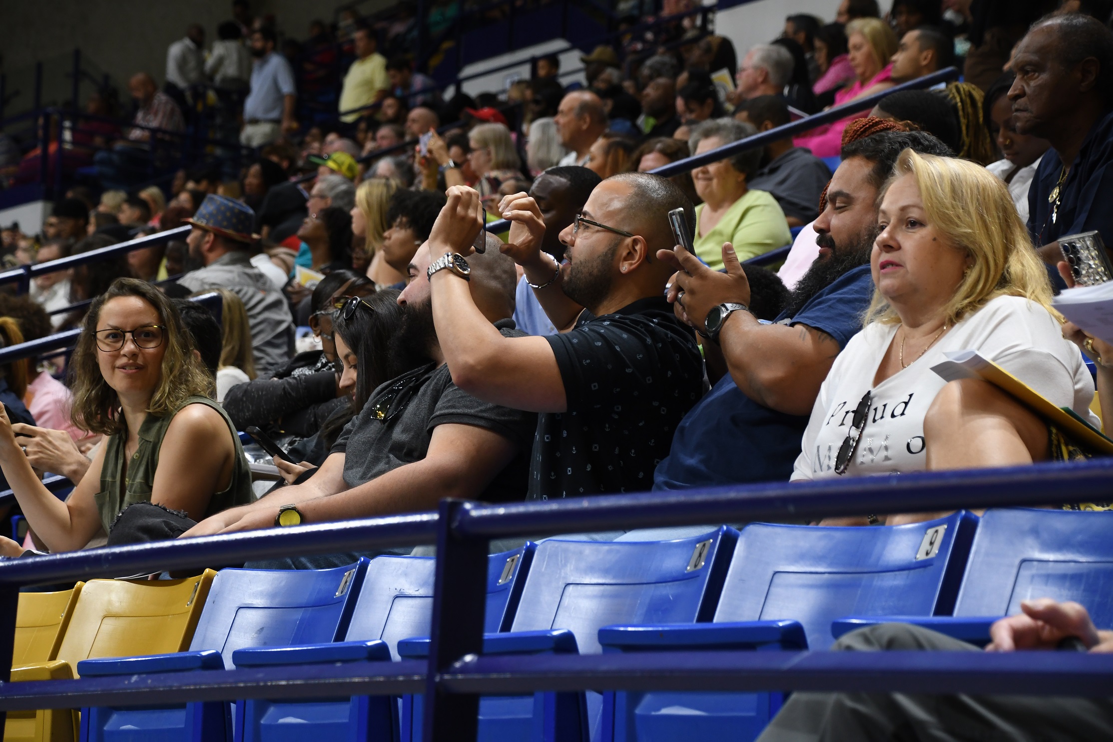 A man, shown in profile, holds up in phone in the stands.