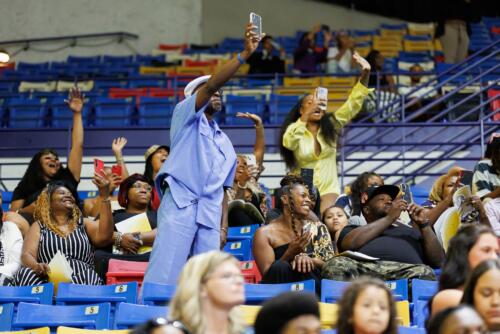 Two people stand and cheer while holding their phones up in the audience.