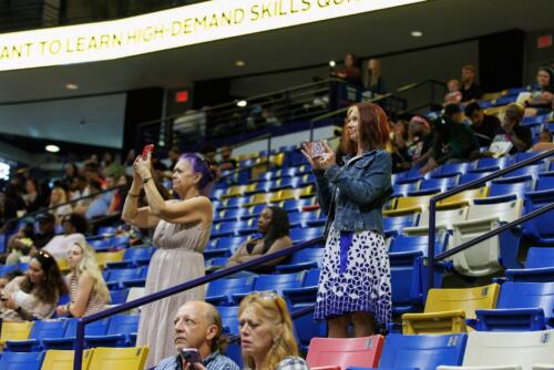 Two women standing in the crowd raise their phones.