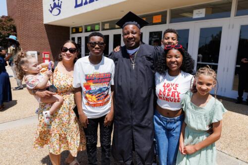 A graduate in his cap and gown stands in the middle of a group of loved ones outside of the Crown Complex doors.